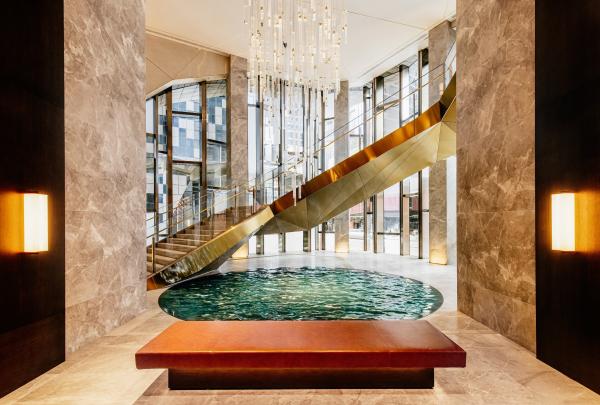 A grand golden staircase spirals past a circular indoor pool beneath a glowing chandelier, part of a luxurious space operated by The Ritz-Carlton, at The Ritz-Carlton, Melbourne, Victoria. © Jon Wah