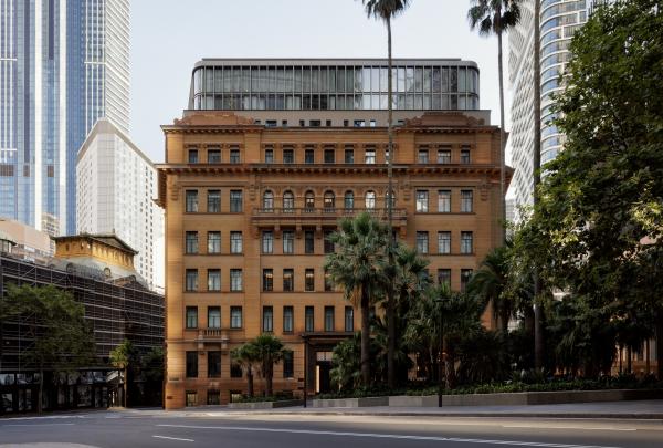 A heritage sandstone building topped with a modern glass extension rises beside palm trees, operated by Capella, at Capella Sydney, Sydney, New South Wales. © Timothy Kaye