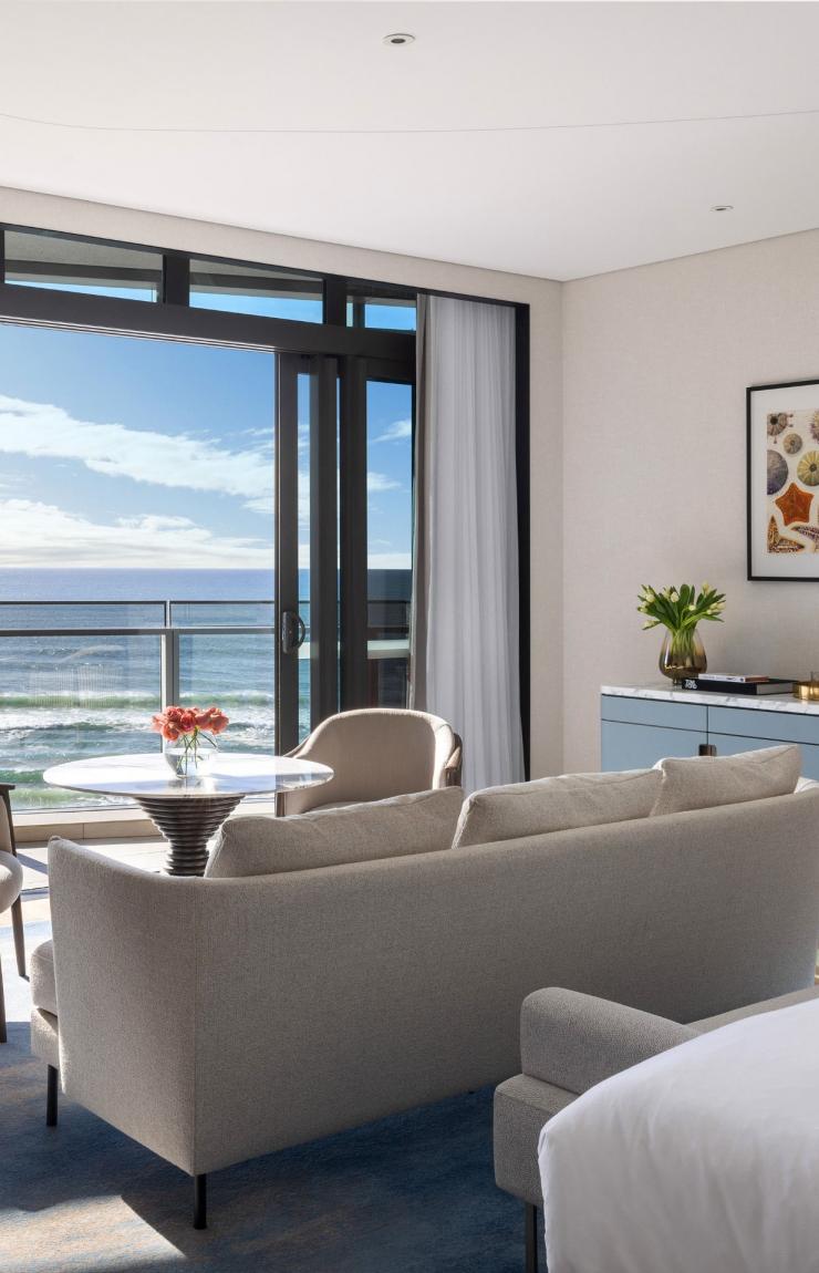 An elegant hotel room featuring a lounge area opens onto a private balcony framing sweeping ocean views, offered by operator The Langham, at The Langham, Gold Coast, Queensland. © The Langham