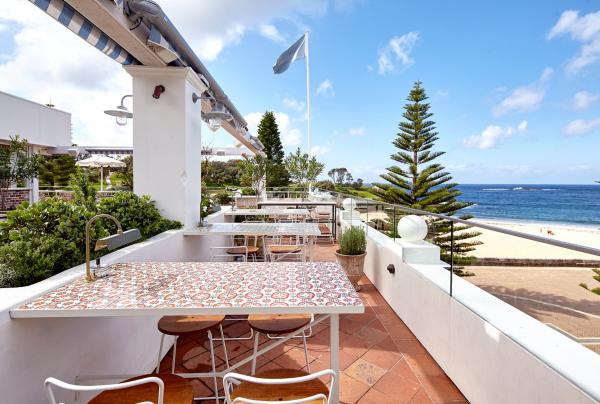 A sunny outdoor terrace features patterned tiled tables and chairs overlooking coastal views and ocean waters at Coogee Pavilion, Sydney, New South Wales. © Coogee Pavilion