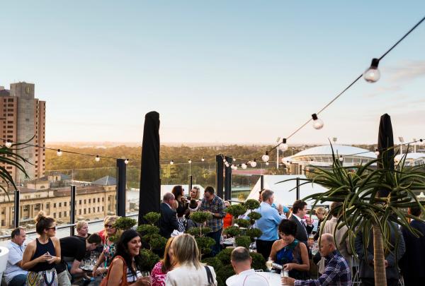 People socialise on a lively rooftop under festoon lights, enjoying sunset views over the city at 2KW Bar and Restaurant, Adelaide, South Australia. © South Australian Tourism Commission