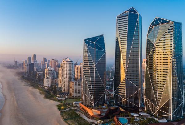 Striking glass towers of The Langham catch the warm golden light, rising dramatically beside a long stretch of sandy beach and coastal skyline, located on the Gold Coast, Queensland.© The Langham