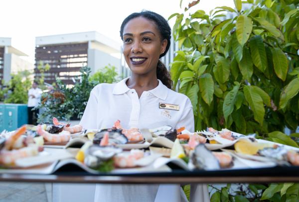 Smiling server holding a platter of fresh seafood canapés including prawns and oysters during the Dreamtime Welcome Event at Crown Towers, Perth, Western Australia. © Tourism Australia