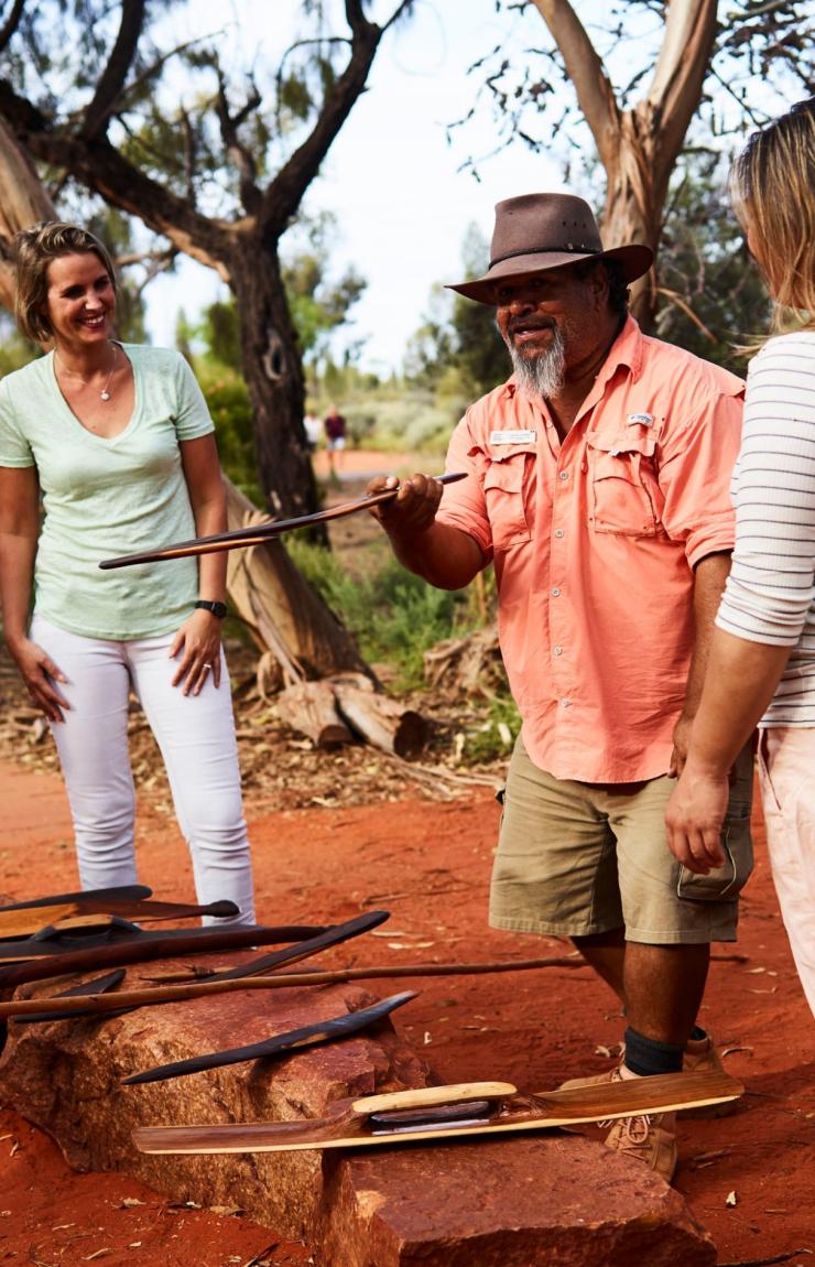 An Aboriginal guide holds traditional tools while speaking to visitors during a Bush Tucker Journey at Ayers Rock Resort, in the Red Centre, Northern Territory. © Voyages