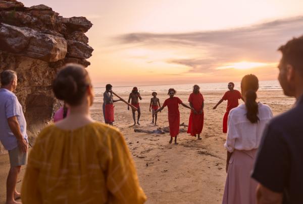 A group watches Indigenous dancers and a didgeridoo player perform near rock formations at sunset on the beach with The Youth Mill, Darwin, Northern Territory. © Northern Territory Business Events