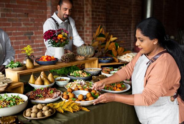 A woman in an apron thoughtfully arranges a platter on a generous grazing table filled with vibrant dishes at Free to Feed, Melbourne, Victoria. © Free to Feed