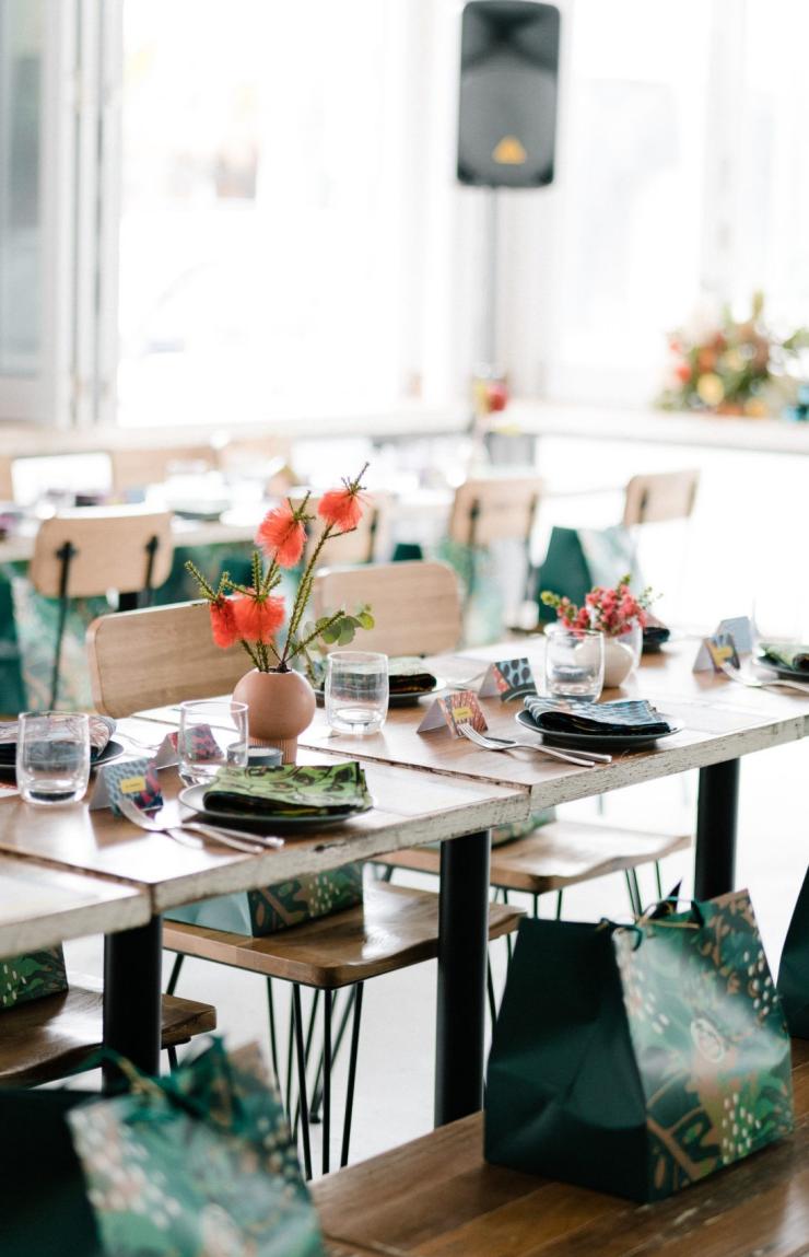 Sunlit dining tables are neatly set with vibrant flower arrangements and gift bags for an event at Heart Cafe in Bondi, Sydney, New South Wales. © Heart Cafe Bondi