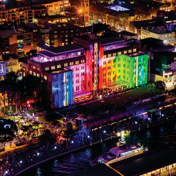 Vibrant, rainbow-coloured light projections illuminate the facade of the grand Museum of Contemporary Art (MCA) building along the harbor at night, Sydney, New South Wales. © Destination NSW