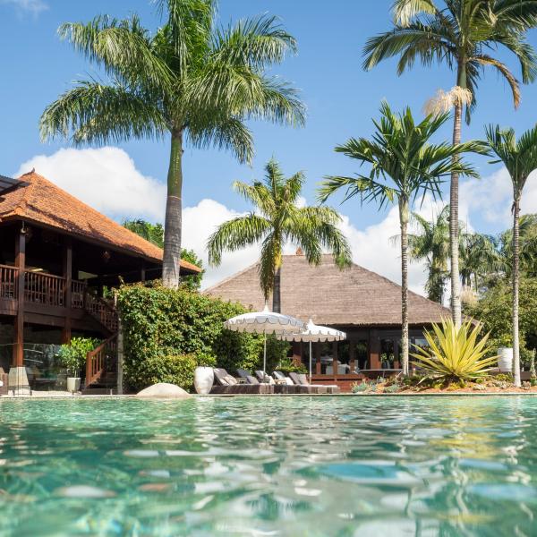 Water ripples gently in a tropical resort pool bordered by soaring palm trees and luxury Balinese-style thatched villas, Makepeace Island, Queensland. © Makepeace Island