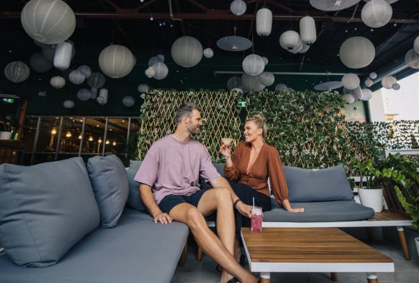 A couple enjoys drinks while relaxing on grey outdoor couches beneath a ceiling covered in white paper lanterns at Charlie's of Darwin in Darwin, Northern Territory © Tourism NT, Backyard Bandits