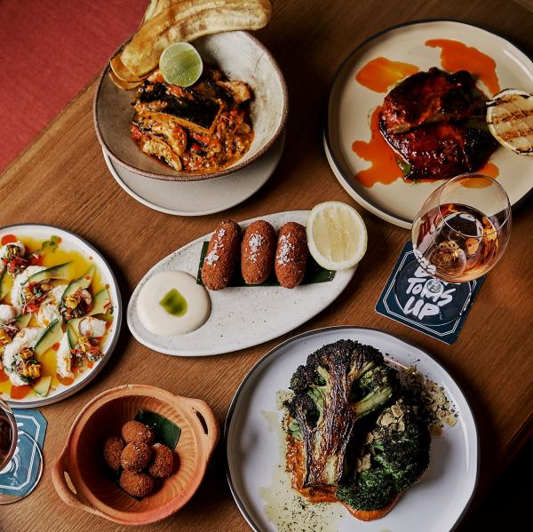Vibrant share plates spread across a wooden table, including roasted broccoli and plantain chips, offering a colourful Latin American dining experience at Lona Misa in Melbourne, Victoria © Lona Misa