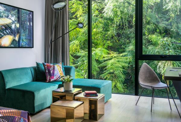 A plush green velvet couch sits beside metallic tables and a window framed by vibrant rainforest foliage, Crystalbrook Vincent, Brisbane, Queensland. © Crystalbrook Vincent