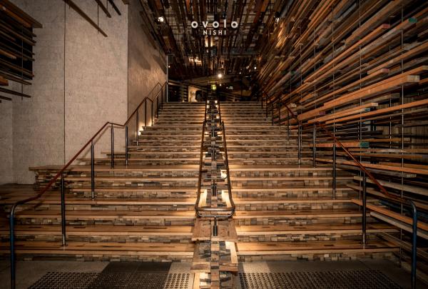 A grand wooden staircase illuminated by warm lights rises through an intricate, sculptural installation of reclaimed timber, Ovolo Nishi, Canberra, Australian Capital Territory. © Simon Casson