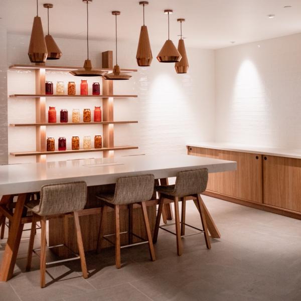 Warm copper pendant lights hang above a sleek kitchen island with tall bar stools and backlit shelves displaying colorful preserved jars, Crowne Plaza Hobart, Tasmania. © Crowne Plaza Hobart