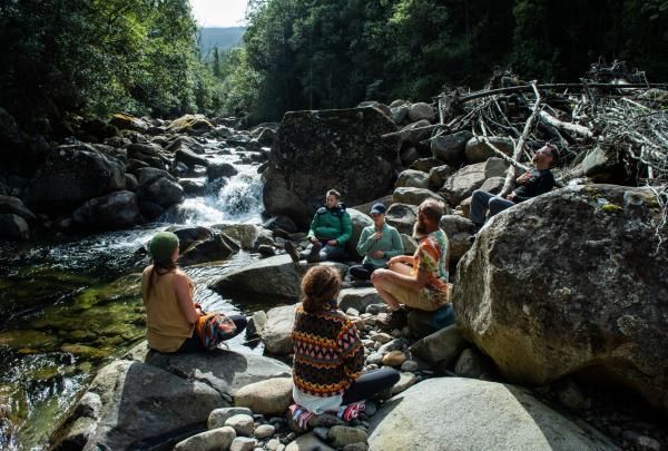 eople meditate together on large rocks beside a rushing mountain stream with Wild Wellness Fire and Ice Walk, Hobart, Tasmania. © Chris Crerar