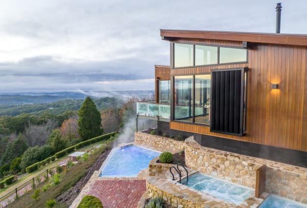 Steam rises from outdoor hot pools set into stone terraces outside a modern luxury lodge overlooking misty hills at Sequoia Lodge, Adelaide, South Australia. © Tourism Australia / Sequoia