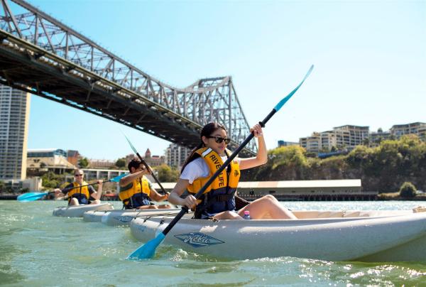 Kayakers row along a sunny river beneath a steel bridge during a guided tour with Riverlife, Brisbane, Queensland. © Riverlife