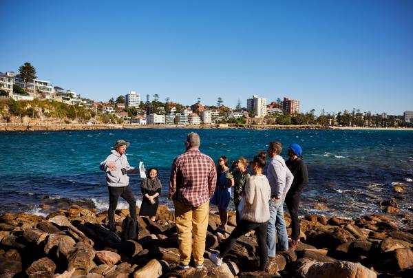 A guide leads a small tour group along a rocky shoreline beside turquoise waters with Eco Treasures, Sydney, New South Wales. © Tourism Australia / Eco Treasures 