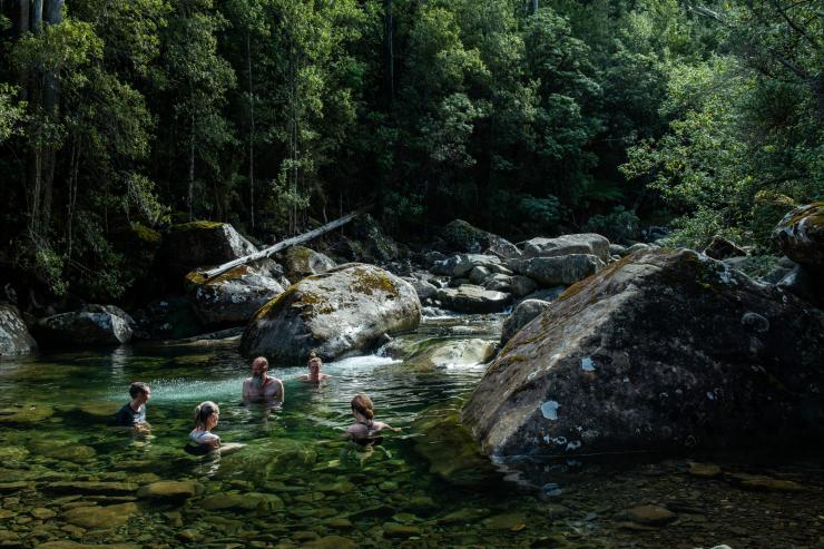 Swimmers cool off in a clear, rocky river pool framed by dense rainforest vegetation with Fire and Ice Walk, Hobart, Tasmania. © Chris Crerar
