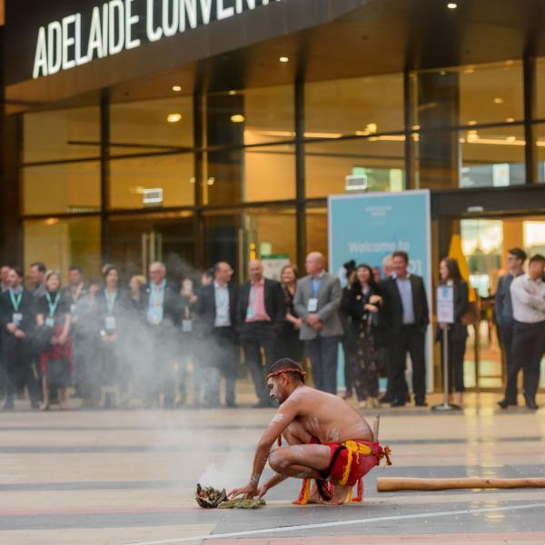 An Indigenous man performs a smoking ceremony in front of a crowd outside the Adelaide Convention Centre, Adelaide, South Australia © Simon Casson