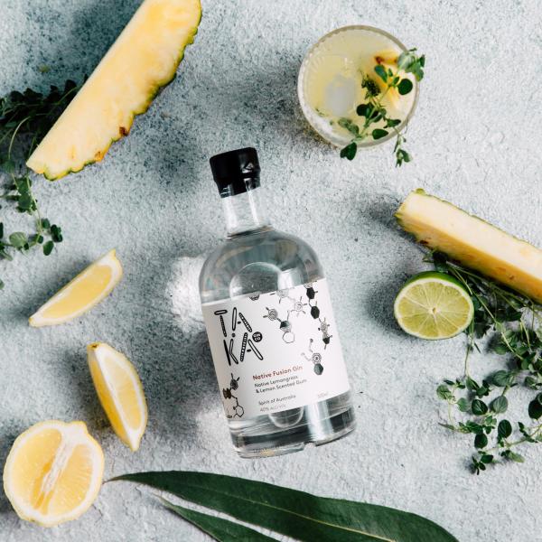 A bottle of Taka Gin displayed flat-lay with fresh pineapple slices, lemon wedges, lime, native herbs, eucalyptus leaves, and a cocktail glass. © Taka Gin