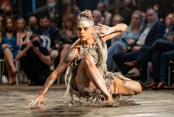 An Indigenous woman with body paint strikes a dramatic low pose during a performance in front of a seated audience at Bangarra Dance Theatre, Sydney, New South Wales © Bangarra Dance Theatre