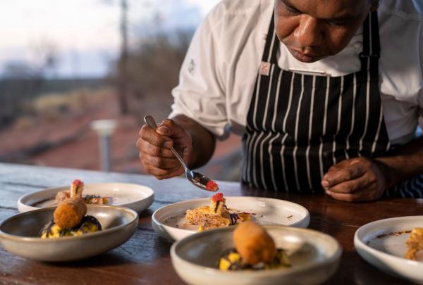 A chef carefully places garnish onto gourmet dishes outdoors against a desert backdrop, Tali Wiru, Ayers Rock Resort, Uluru-Kata Tjuta National Park, Northern Territory. © Ayers Rock Resort