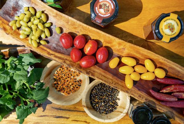 A vibrant spread of fresh produce displayed on a wooden platter in Caversham, Swan Valley, Western Australia. Native bush foods, colourful tomatoes, and local produce jars feature in full sunlight. © Tourism Australia