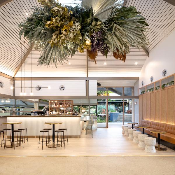 A stylish dining space at Botanic House, Sydney, New South Wales, featuring high angled ceilings, a lush botanical installation overhead, warm timber accents, and soft, inviting interior lighting. © Botanic House