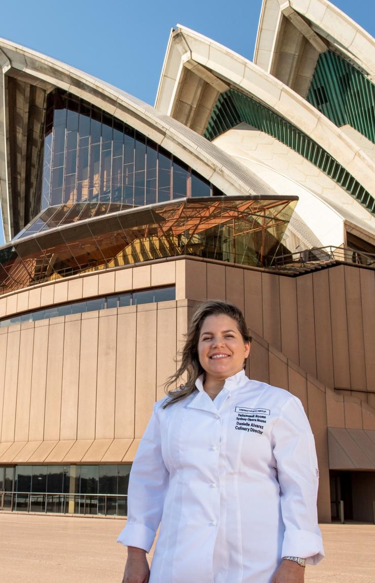 Chef Danielle Alvarez standing proudly in front of the iconic white sails of the Sydney Opera House under a clear blue sky in Sydney, New South Wales, wearing a white chef jacket and smiling warmly. © Danielle Alvarez