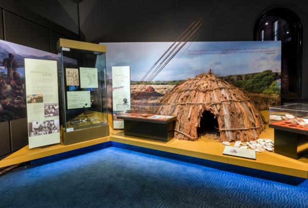 A traditional bark dome hut and spears are displayed on a yellow platform in the ningina tunapri Gallery, Tasmanian Museum and Art Gallery, Hobart, Tasmania. © Tasmanian Art Gallery and Museum