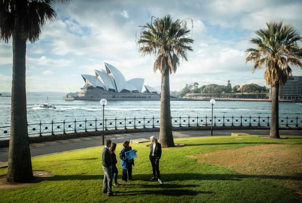 A guide speaks with a small group on a harbourfront lawn opposite the Sydney Opera House during a Dreamtime Southern X tour, Sydney, New South Wales. © Tourism Australia