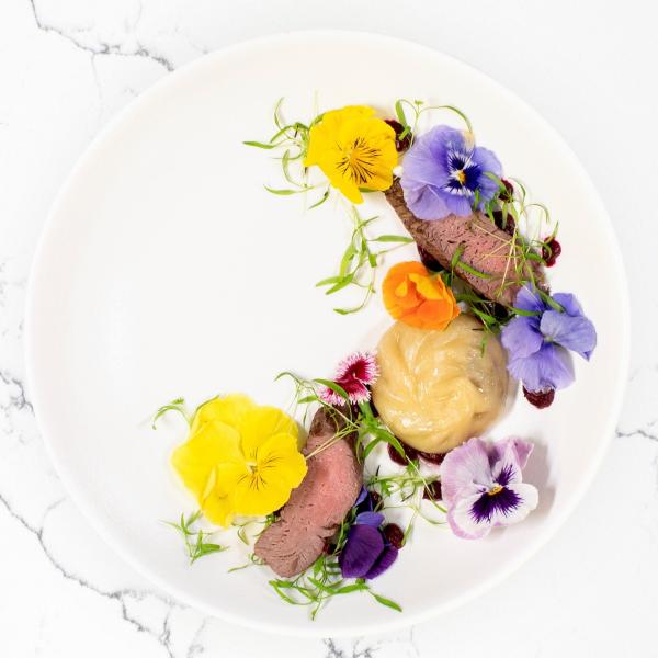Slices of tender meat, a steamed dumpling, and vibrant edible flowers are arranged in a curve on a white plate at Darwin Convention Centre, Darwin, Northern Territory. © Darwin Convention Centre
