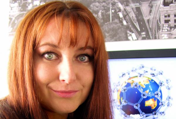 Dr Amanda Barnard smiles beside a computer screen displaying a 3D molecular globe model in a study. © Dr Amanda Barnard
