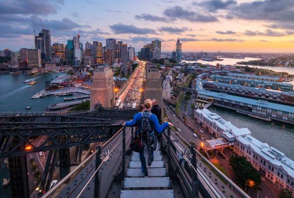 Climbers ascend the metal catwalks of the Sydney Harbour Bridge during twilight, overlooking the illuminated city skyline with BridgeClimb Sydney, New South Wales. © Destination New South Wales
