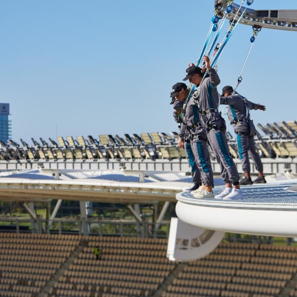 Guests in safety harnesses lean out from the edge of the high roof platform during a stadium roof climb experience at Optus Stadium, Perth, Western Australia. © Travis Hayto