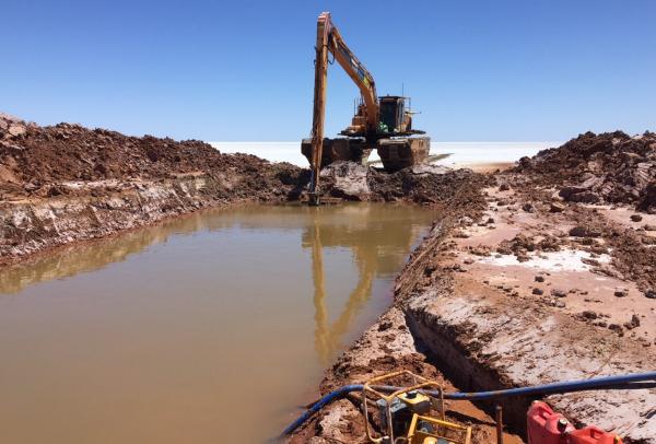 An Agrimin amphibious excavator digs a long, water-filled trial trench for pump testing across a vast salt lake bed, Western Australia. © Agrimin
