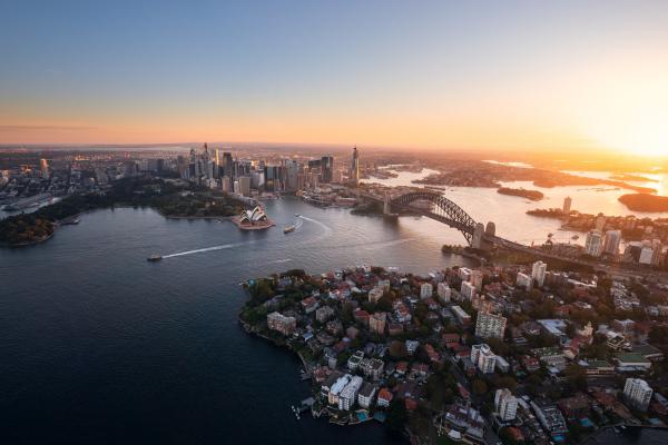 A breathtaking aerial view captures the sun setting over the iconic Sydney Opera House and Sydney Harbour Bridge spanning across sparkling blue waters of Sydney Harbour, New South Wales. © Daniel Tran