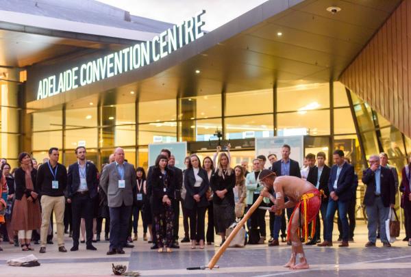 An Indigenous performer plays the didgeridoo before a crowd gathered outside the glass entrance of the Adelaide Convention Centre, Adelaide, South Australia. © Simon Casson