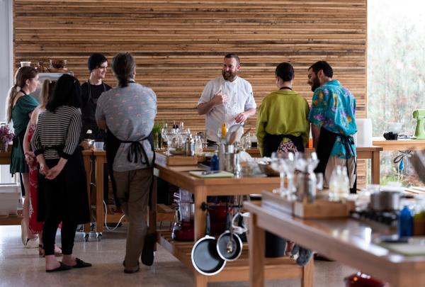 A chef leads a cooking demonstration for a group around a wooden kitchen island at Maggie Beer’s Farm Shop, Barossa Valley, South Australia. © Pete Thornton