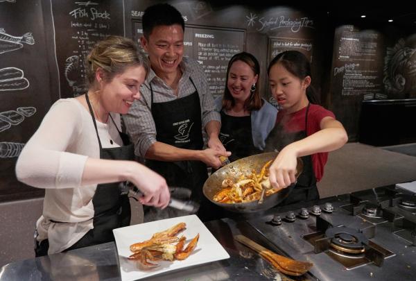 Four people cook crab together, tossing ingredients in a wok and plating seafood at Sydney Seafood School, Sydney, New South Wales. © Franz Scheurer