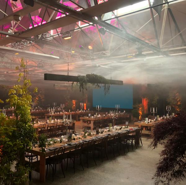 Atmospheric banquet setup at Princes Wharf No. 1, with long wooden tables, lush greenery and misty ambient lighting in Hobart, Tasmania. © Tourism Australia
