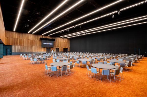 A spacious, modern event hall at CENTREPIECE set up with numerous round tables, grey chairs, orange carpeting, and sleek linear ceiling lights, located in Melbourne, Victoria. © Richard Timbury