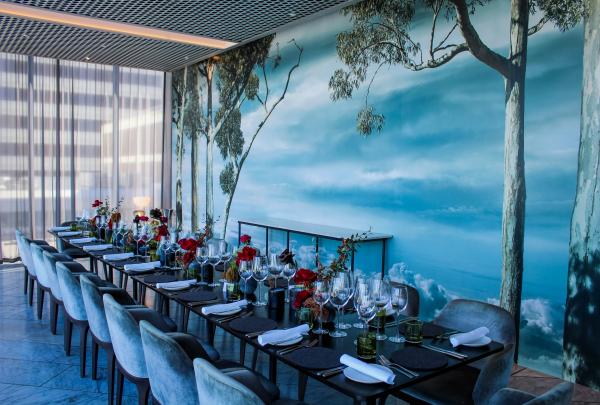 A long dining table set with red floral arrangements stands beside a blue forest mural, Wildflower private dining room, COMO The Treasury, Perth, Western Australia. © COMO The Treasury