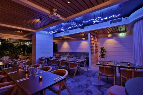 Blue neon lights glow above elegant dining tables set for dinner in a stylish, moody restaurant space, The Rimini Room, Miss Moneypenny’s, Gold Coast, Queensland. © Christopher Cypert