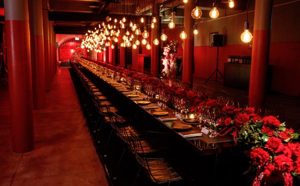Warm pendant lights illuminate a long, dramatic banquet table adorned with vibrant red roses inside a moody cellar room, Penfolds Dining Room, Adelaide, South Australia. © Penfolds