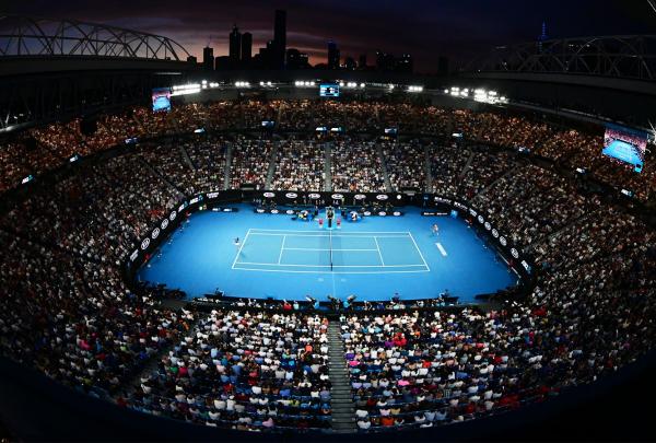 High-angle stadium view of a night tennis match on a blue court at the Australian Open surrounded by a packed crowd, Melbourne, Victoria. © Tourism Australia