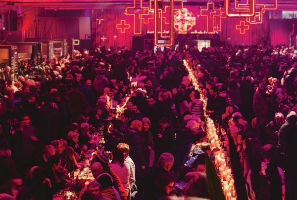 A large crowd dines at long tables illuminated by glowing red cross lights during the Dark Mofo Festival in Hobart, Tasmania. © Adam Gibson
