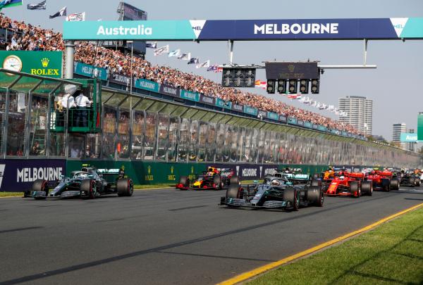 Formula One cars speed past crowded grandstands under an overhead sign at the Australian Grand Prix in Melbourne, Victoria. © Steven Tee
