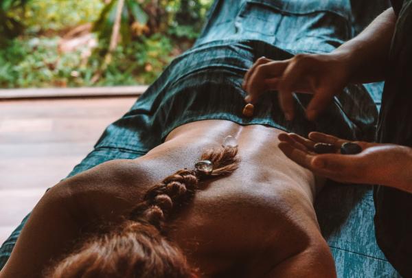 A guest receives a relaxing stone massage treatment inside an open-air pavilion surrounded by lush rainforest greenery at Silky Oaks Lodge in Queensland. © Tourism and Events Queensland and Katie Purling